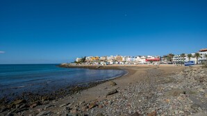 A rocky beach with a town in the background. - Sunset Arguineguin by CanariasGetway (Mogán)