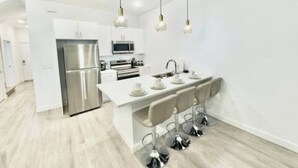 Een moderne keuken met een centraal eiland, roestvrijstalen apparatuur en hangende lampen.