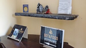 A wooden table with a sign for 'BotaFogo Ristorante' and a shelf above it with a menu and a small decorative pine cone arrangement. - Room 'Camera Matrimoniale' with Shared Garden, Wi-Fi and Air Conditioning (Chiavari)