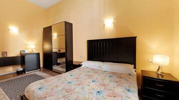 A hotel room with a bed, a nightstand, a dresser, a mirror, and a wall-mounted light.
