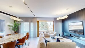 En moderne stue med spiseplads, sofa, tv og et stort vindue med gardiner.