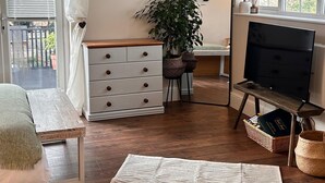 A room with a wooden floor, a white sofa, a white dresser, a black TV stand, a large woven rug, a potted plant, and a framed picture on the wall.