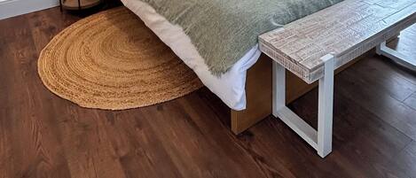 A bedroom with a wooden bed, a round woven rug, a bench, and a ceiling fan.