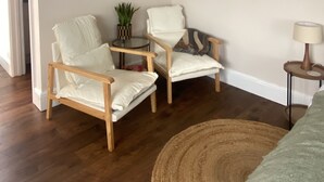 A room with two white armchairs, a small table with a plant, a lamp, and a woven rug.