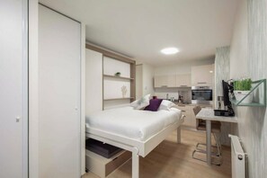 Ein kleines Schlafzimmer mit einem Bett, einem Schreibtisch und einer Küchenzeile.