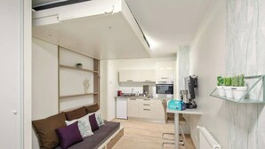 A compact living space with a kitchenette, a sofa with cushions, and a small dining area. - Beautiful and modern studio for 2 near Bastille (Paris)