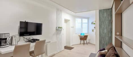 A modern living room with a flat-screen TV, a coffee machine, and a dining area with a table and chairs.