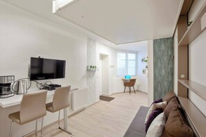 A modern living room with a flat-screen TV, a coffee machine, and a dining area with a table and chairs.