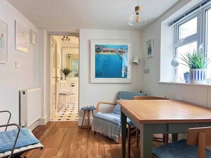 A cozy, well-lit room with a wooden dining table, a blue-striped chair, and a view of the sea through a window. - Cozy One-Bedroom Apartment Near Brighton Seafront (Brighton)