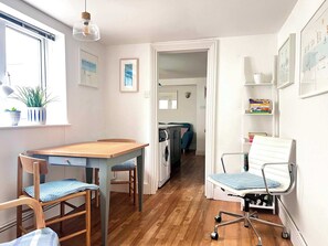 Un espacio habitable compacto con comedor, kitchenette y una pequeña zona de estar con una silla y un banco.