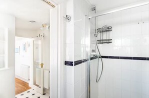 Un baño moderno con baldosas blancas, una cabina de ducha de vidrio y un suelo con estampado blanco y negro.