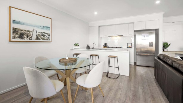 A modern kitchen with white cabinets, a stainless steel refrigerator, and a dining area with a glass table and white chairs. - Cherry St Retreat, Armstrong Creek (Armstrong Creek)