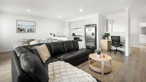 A modern living room with a black leather sofa, a round coffee table, and a dining area with a white table and chairs. - Cherry St Retreat, Armstrong Creek (Armstrong Creek)