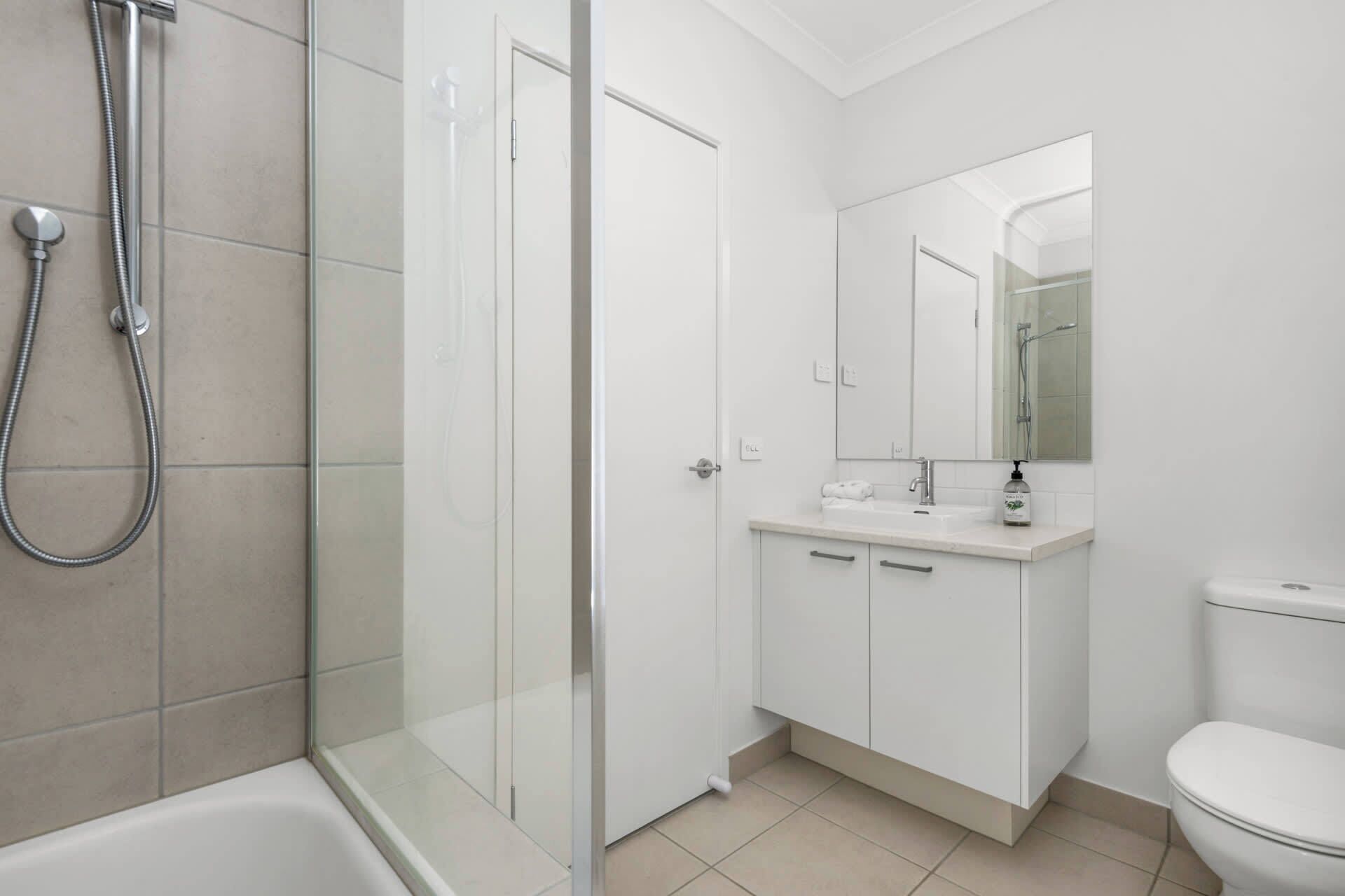 Un baño moderno con ducha de vidrio, inodoro blanco y lavamanos con espejo.