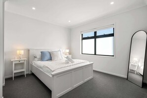 A modern bedroom with a white bed, grey carpet, a large window, and a mirror. - Cherry St Retreat, Armstrong Creek (Armstrong Creek)