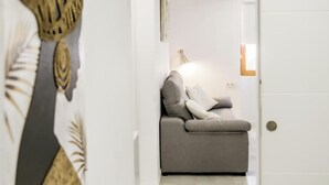 A modern living room with a grey sofa, a lamp, and a wall with a decorative piece. - Catalina Suites Downtown Valencia (València)