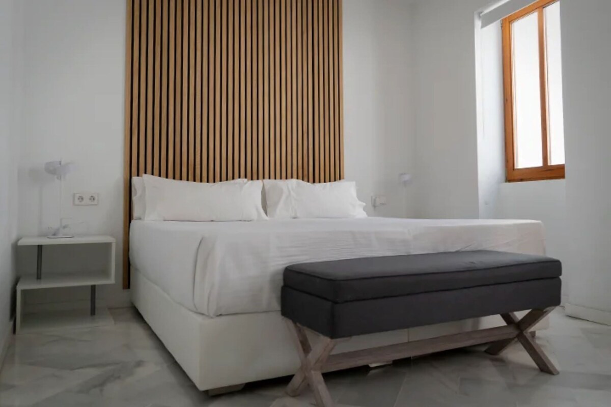 A modern bedroom with a bed, bedside tables, a window, and a wooden slat wall.