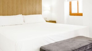 A neatly made bed with white linens, a wooden headboard, and a small bedside table with a lamp. - Catalina Suites Downtown Valencia (València)