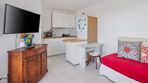 A compact room with a bed, a desk, a TV, and a kitchenette. - 2-Room Apartment with Sea View Terrace, Balcony, and Air Conditioning (Cavalaire-sur-Mer)