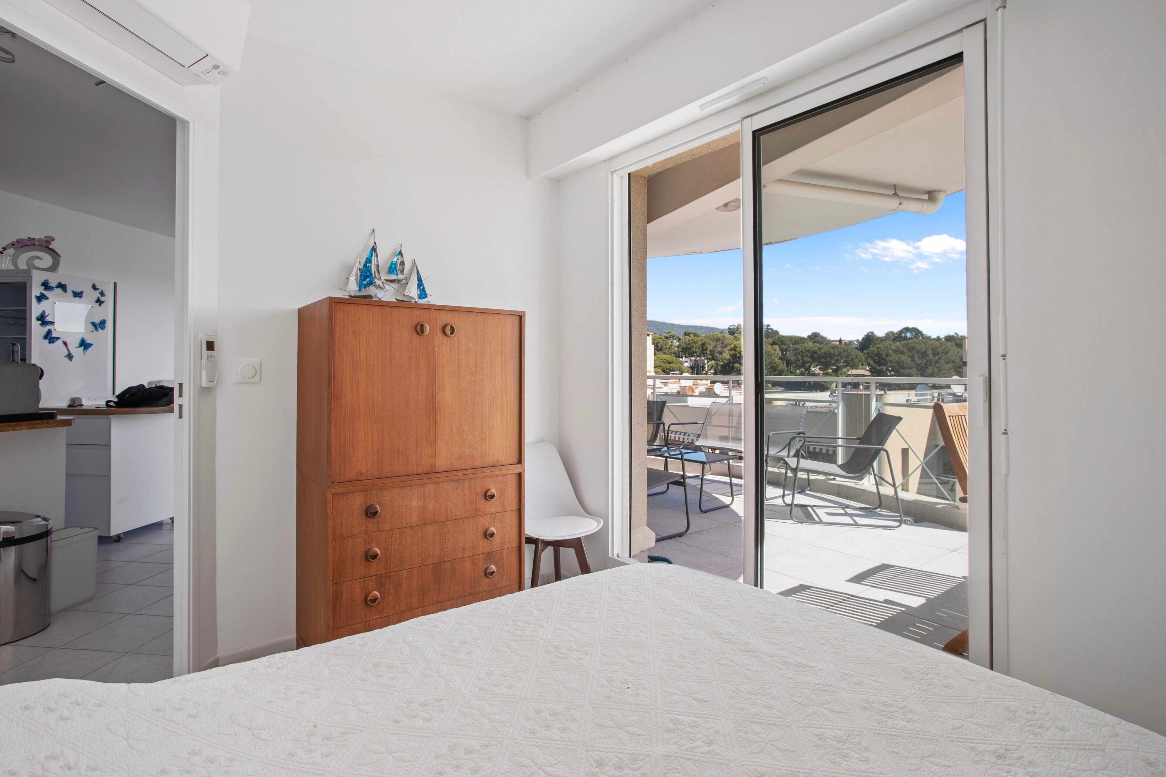 Ein Schlafzimmer mit einem Bett, einem Holzschrank, einem weißen Stuhl und einem Balkon mit Gartenmöbeln.