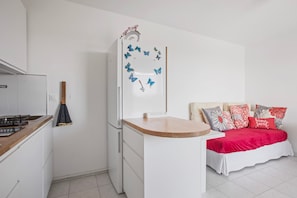 A compact kitchen with a refrigerator, a wooden countertop, and a bed with a red bedspread and decorative pillows.