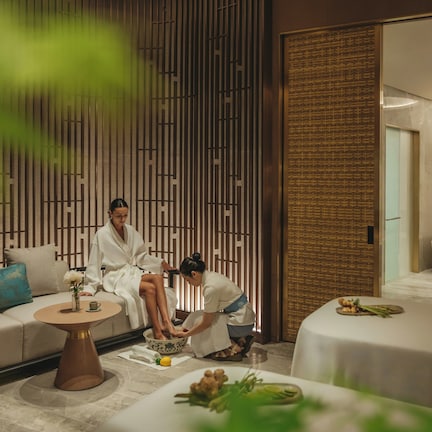 A spa room with a sofa, a round table with a bowl, a sink, and a wall with vertical lines.