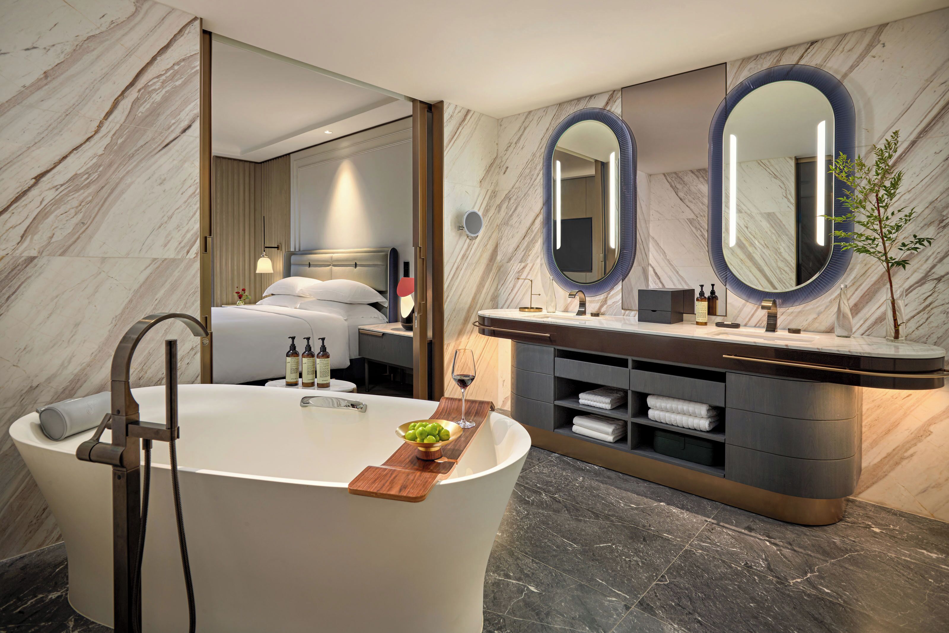 A modern bathroom with a freestanding bathtub, a vanity with a mirror, and a bedside table with a lamp.