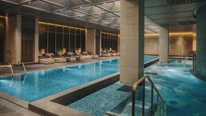 A modern indoor swimming pool with lounge chairs and a separate hot tub area. - Fairmont Hanoi (Hanoi)