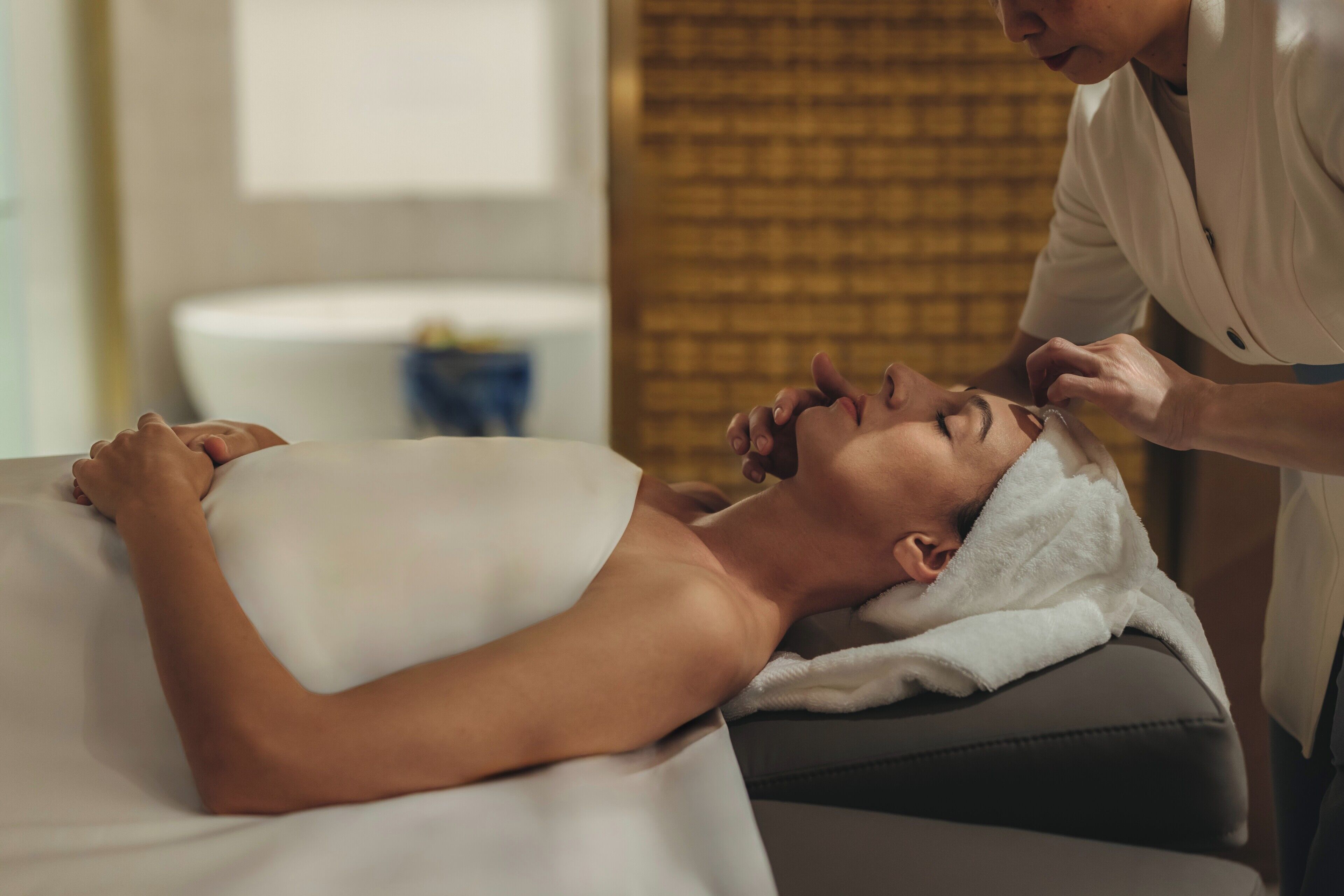 A person lying on a massage table in a room with a brick wall and a white sink in the background.