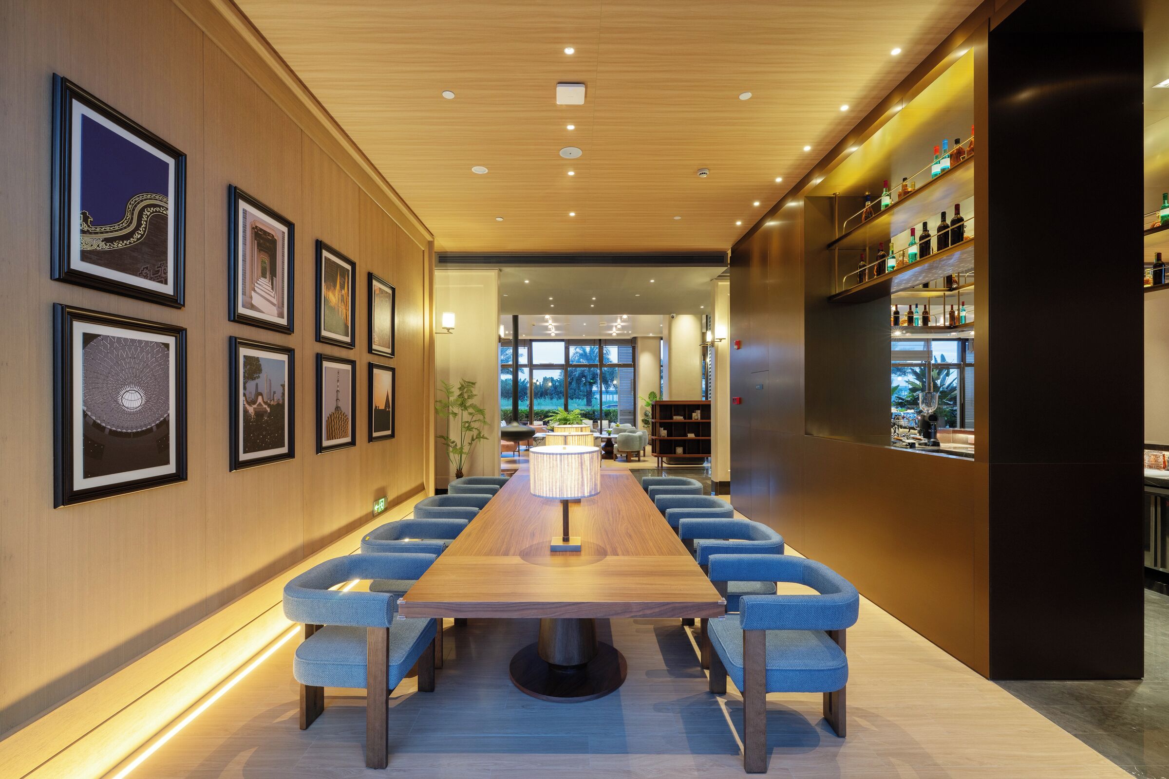 Uma longa mesa de jantar com cadeiras azuis, obras de arte nas paredes e um bar com prateleiras cheias de garrafas.