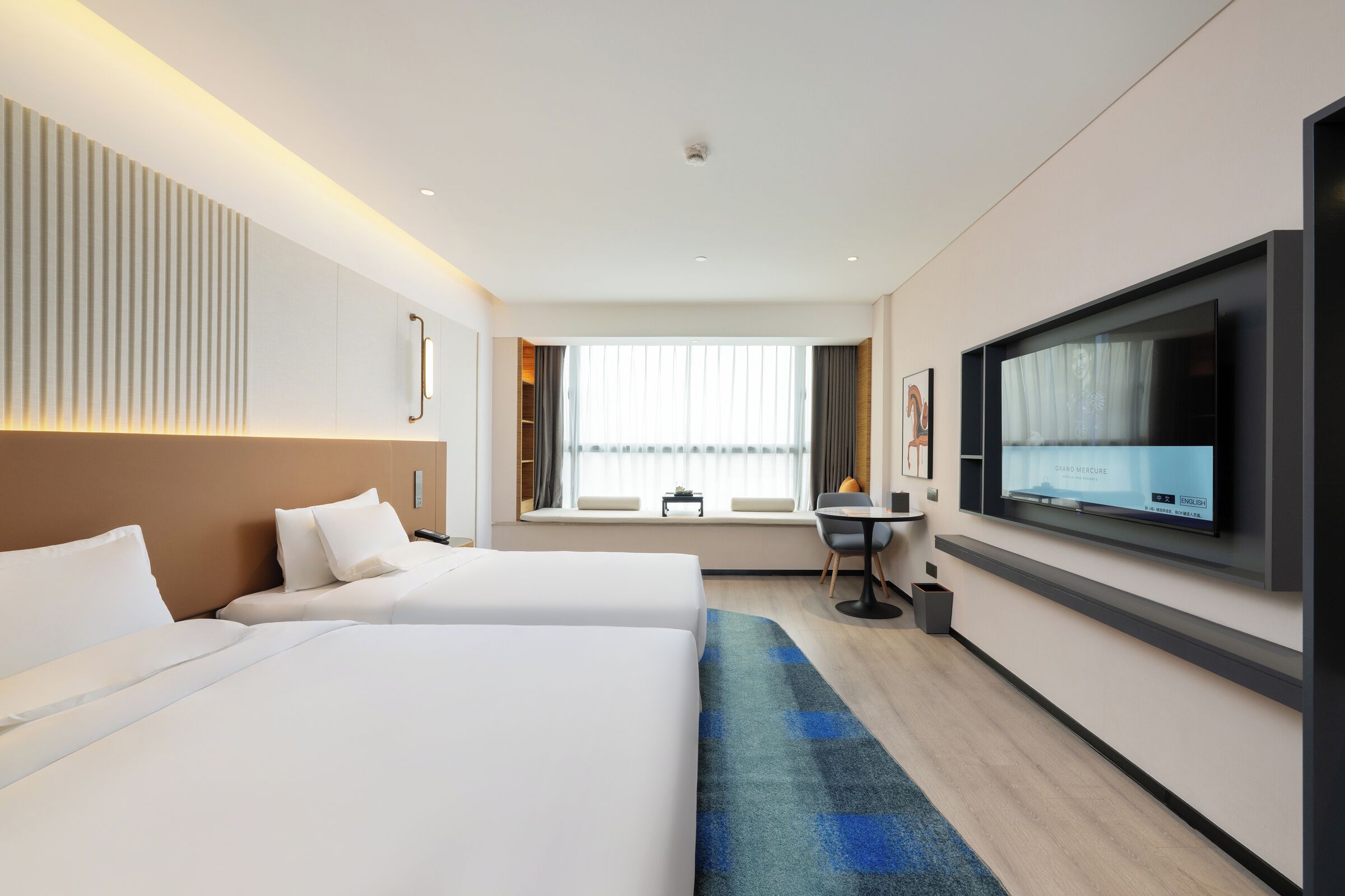 Habitación de hotel con dos camas, televisión, escritorio y ventana con cortinas.