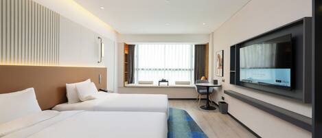 Habitación de hotel con dos camas, televisión, escritorio y ventana con cortinas.