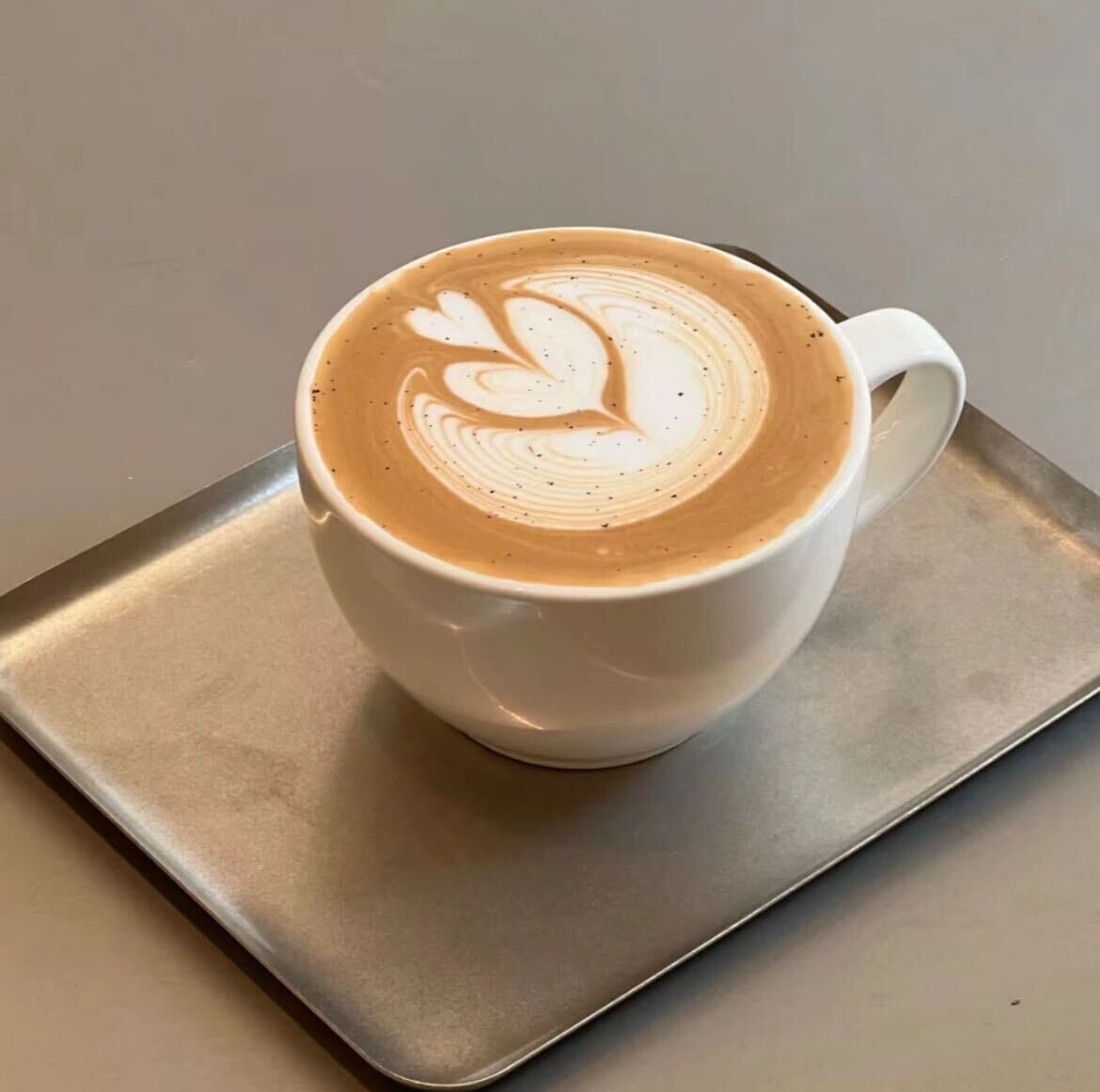 A white cup of coffee with latte art on a metal tray.