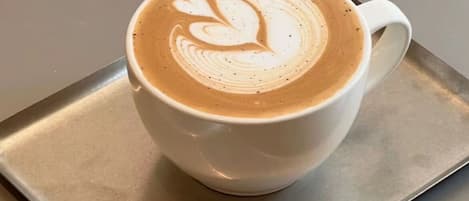 A white cup of coffee with latte art on a metal tray.