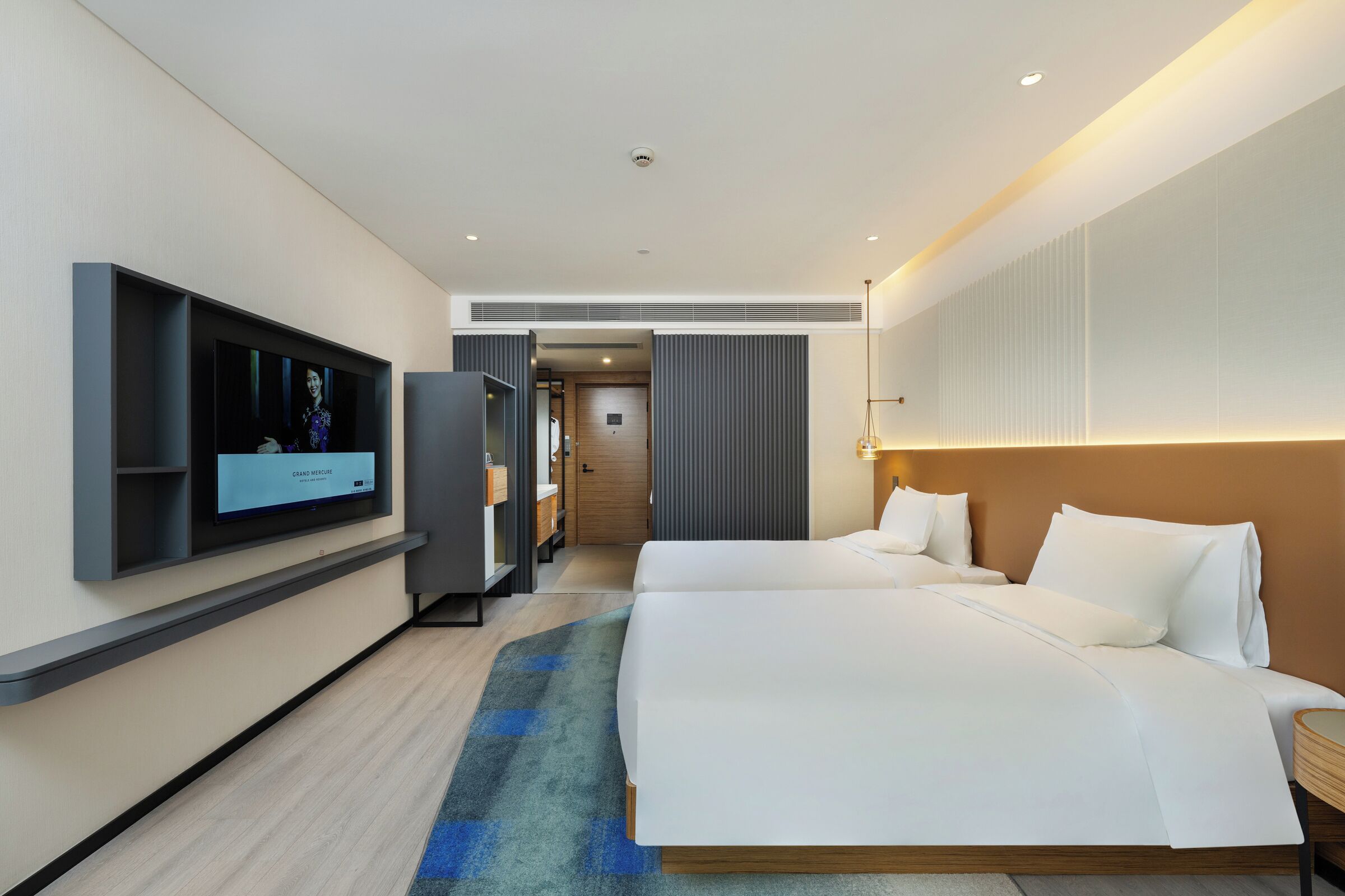 A hotel room with a large bed, a TV mounted on the wall, and a wooden floor.