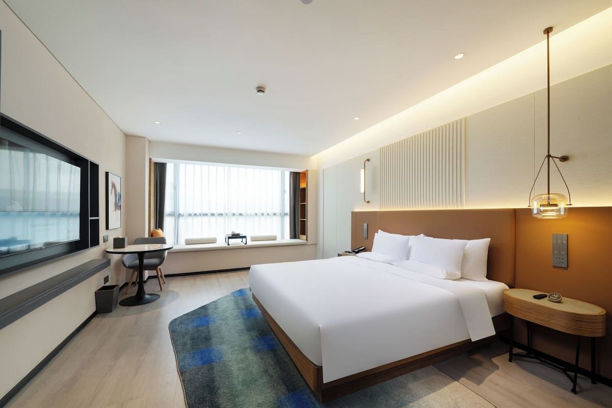 Een moderne hotelkamer met een groot bed, een bureau en een raam met zonwering.