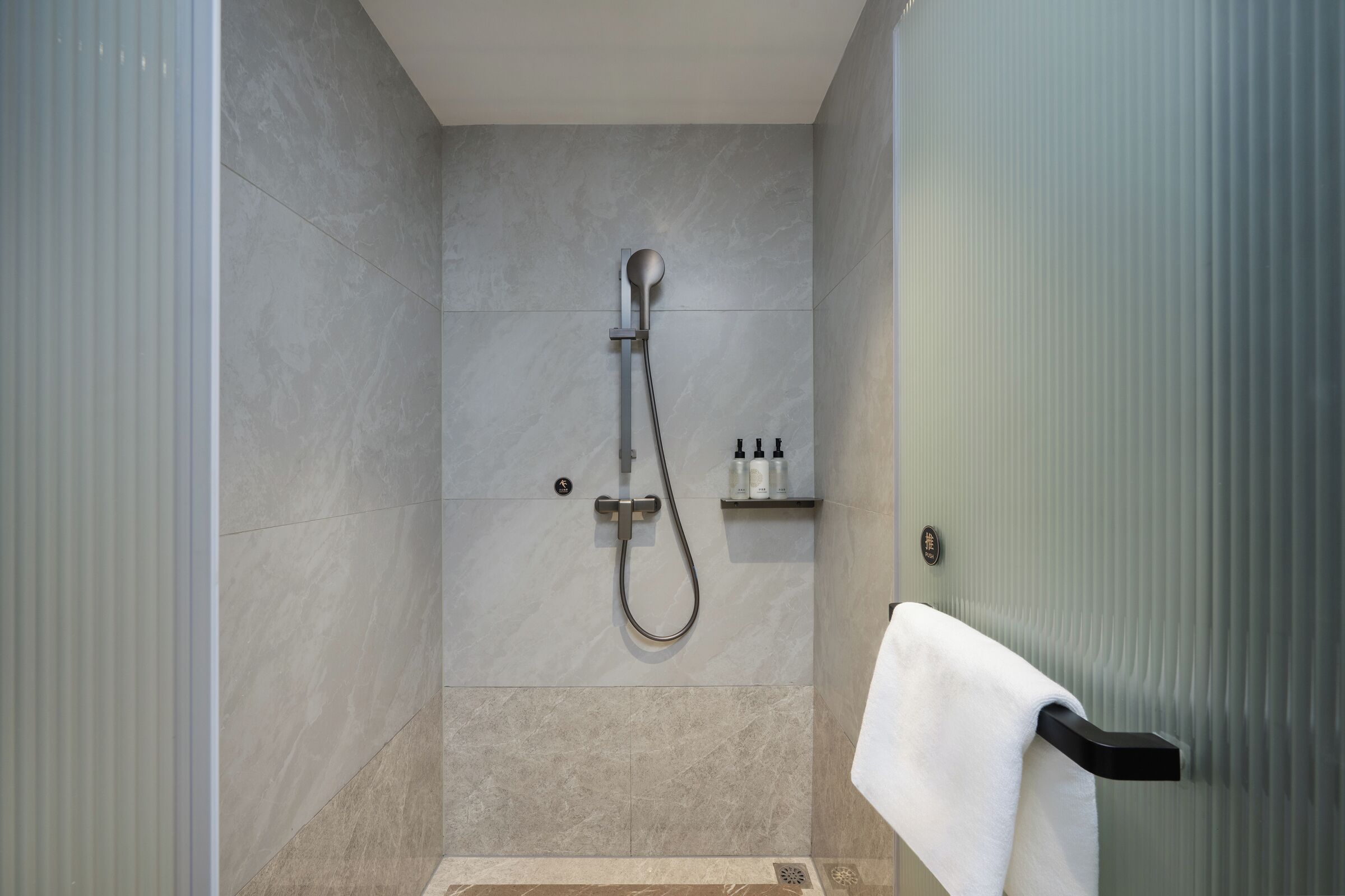 A shower with a handheld showerhead, a towel rack, and a shelf with toiletries.