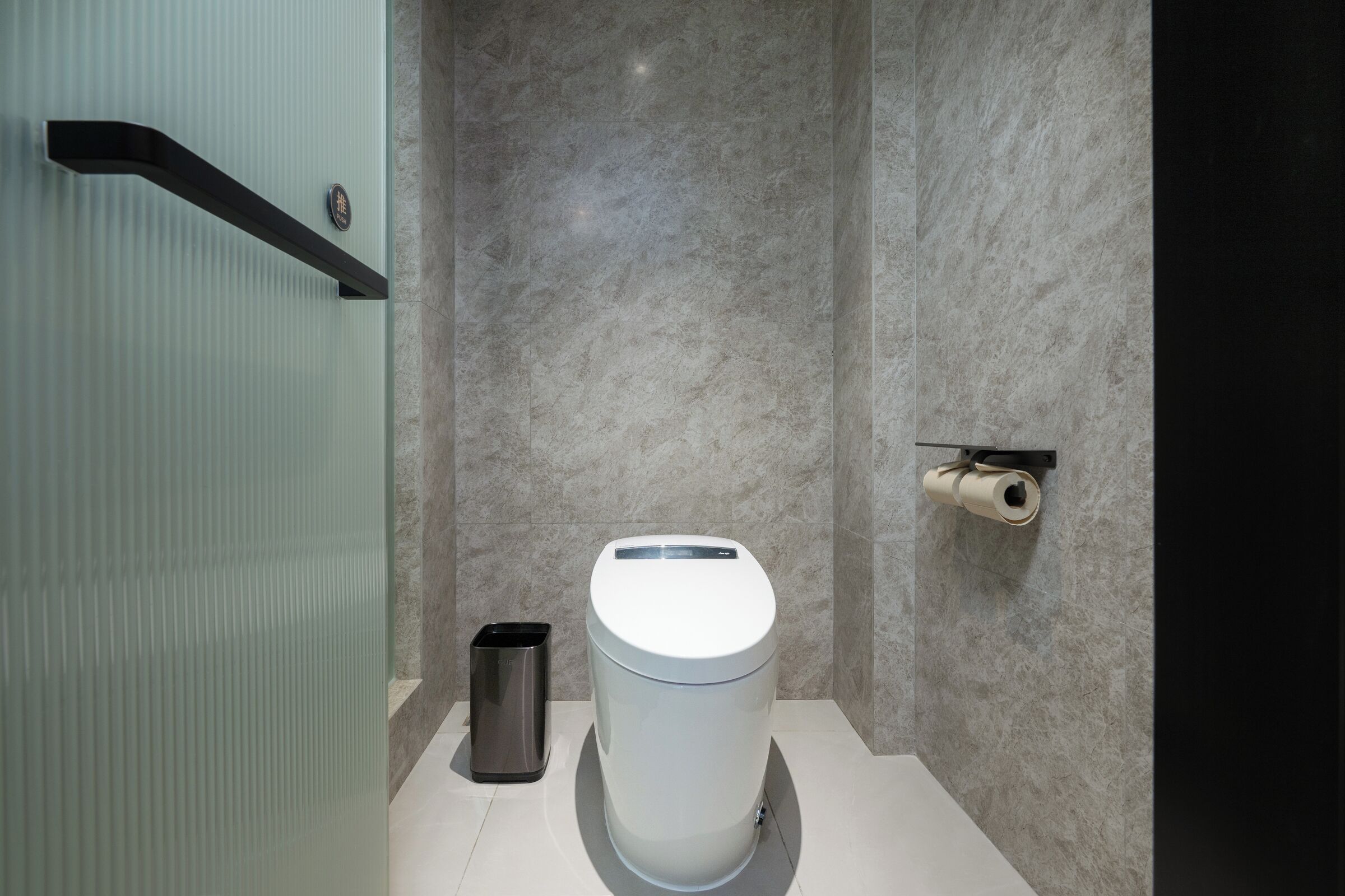 Een moderne badkamer met toilet, prullenbak en toiletrolhouder aan de muur.