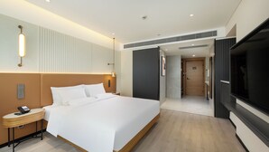Une chambre d’hôtel moderne avec un grand lit, une table de chevet avec un téléphone, une télévision et une porte donnant accès à une salle de bain.