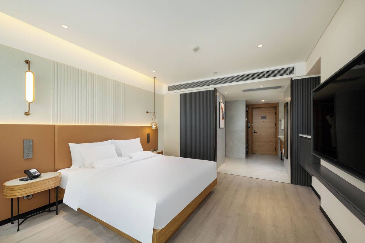 Een moderne hotelkamer met een groot bed, nachtkastje met een telefoon, een televisie en een deur naar een badkamer.