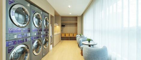A laundry area with multiple washing machines, a seating area with chairs, and a view of the outside through large windows.