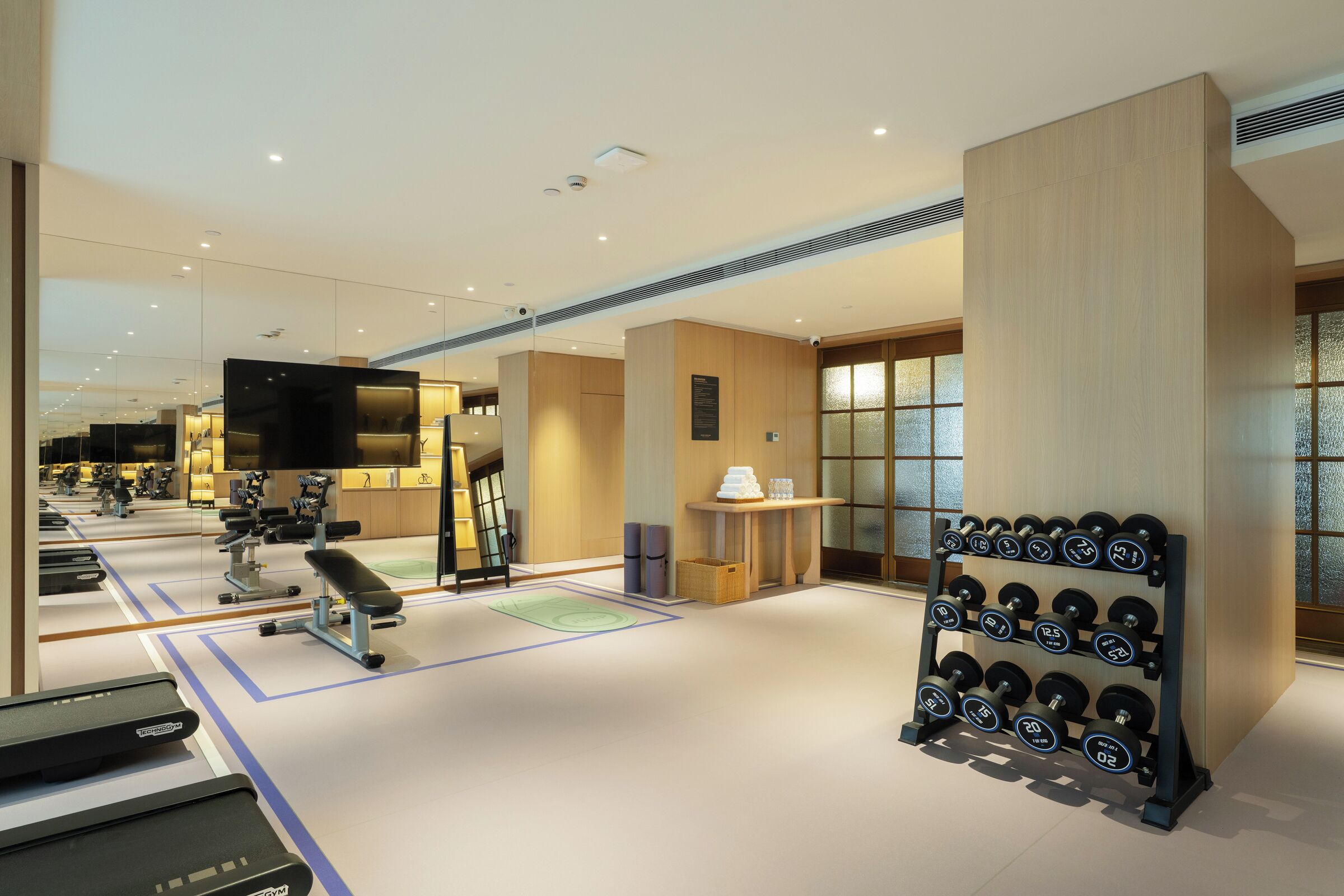 A modern gym with exercise equipment, a wall-mounted TV, and a rack of dumbbells.