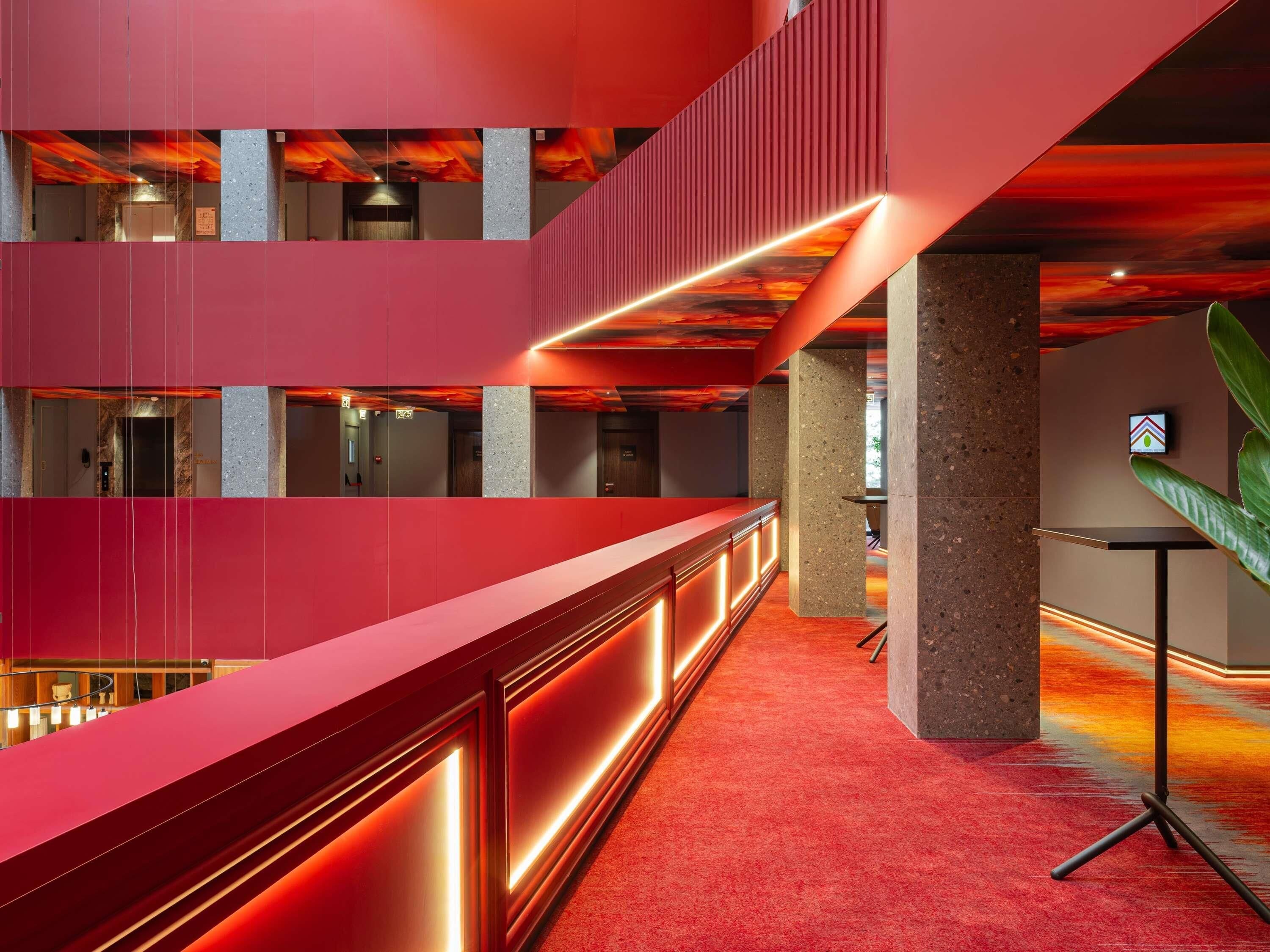 A modern interior with a red reception desk, multiple floors, and a view of the sky through the ceiling.