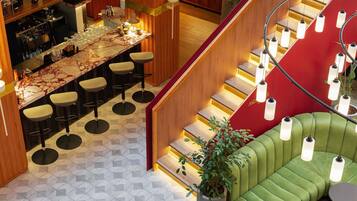 Zona bar moderna con bancone in marmo, sgabelli da bar e una scala con dettagli rossi.