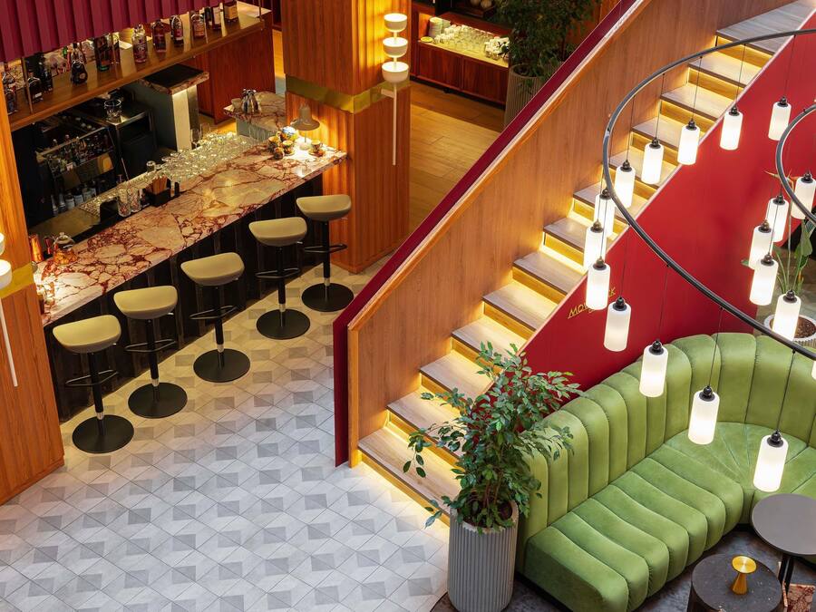 Zona bar moderna con bancone in marmo, sgabelli da bar e una scala con dettagli rossi.
