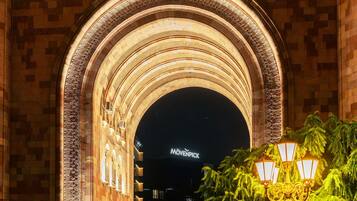 An arched architectural feature with intricate carvings, a sign reading 'MÖVENPICK,' and a street lamp with greenery in the foreground.