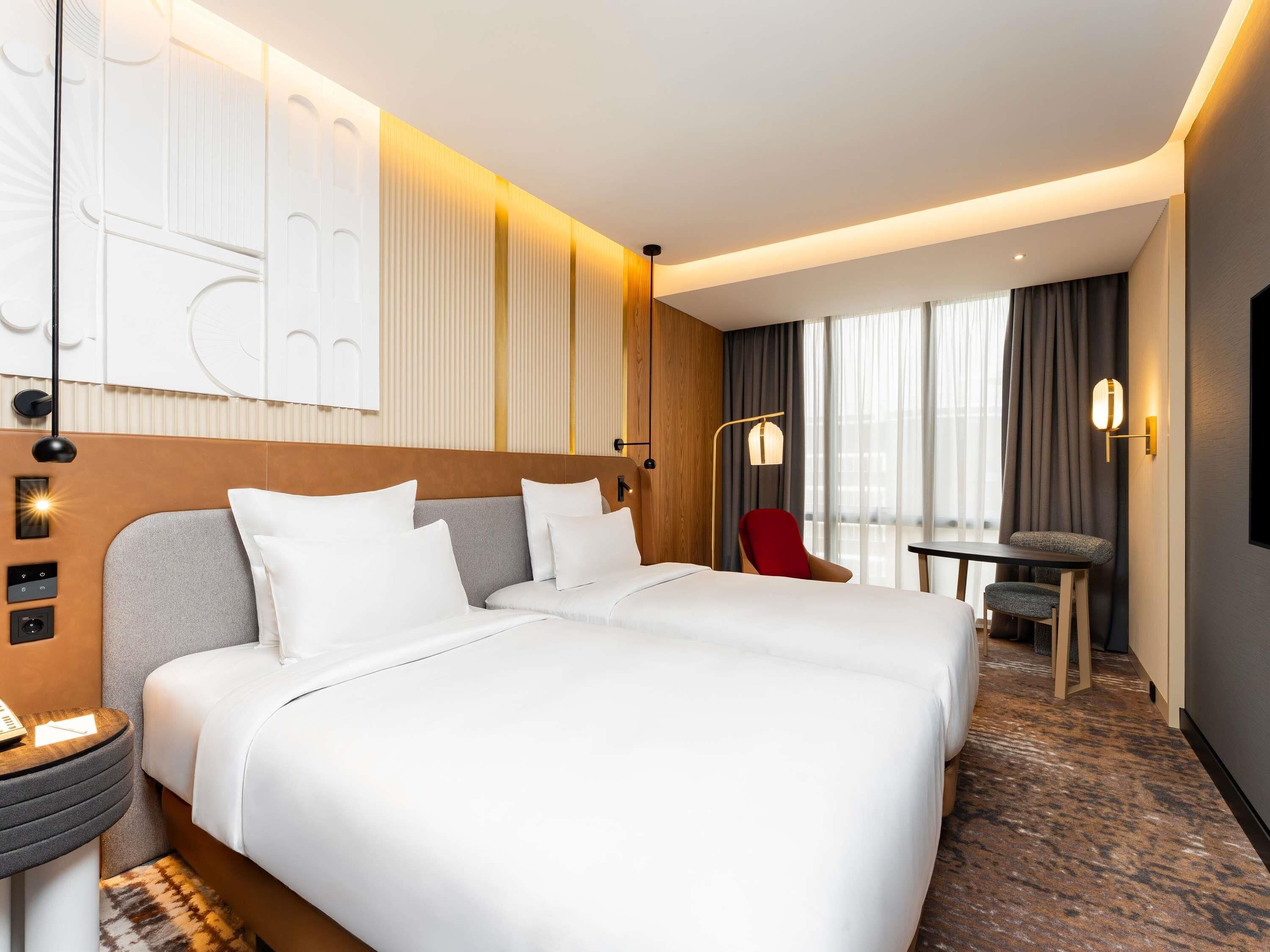 Een hotelkamer met een groot bed, een bureau, een stoel en uitzicht op de stad.