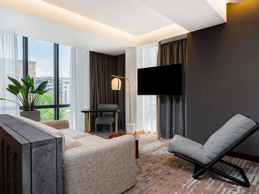 Una sala de estar moderna con un sofá, un sillón, un televisor de pantalla plana y un ventanal con cortinas.