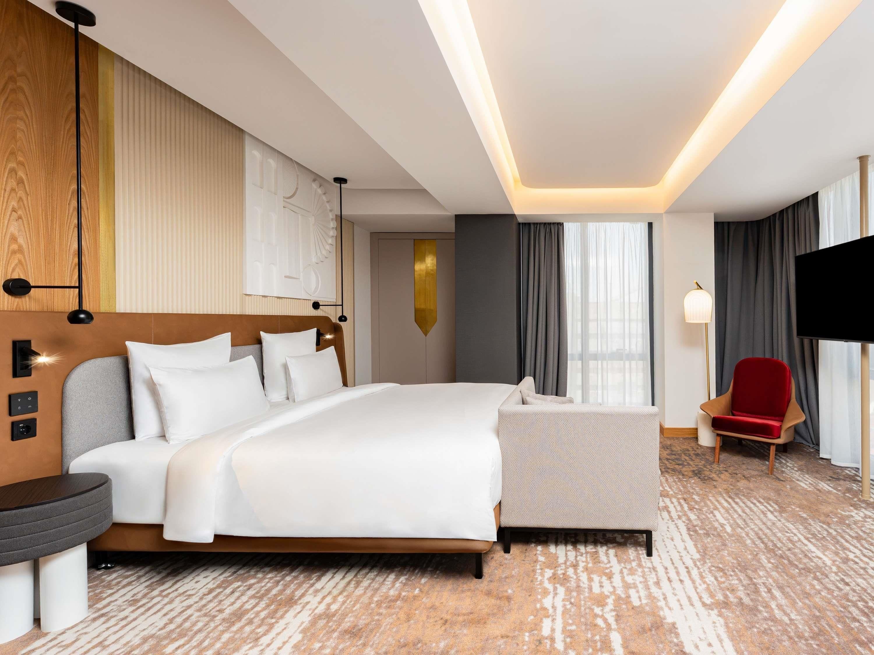 Una camera d'albergo con un letto grande, una televisione, una poltrona rossa e un tappeto decorato.