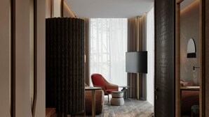A hotel room with a large window, a flat-screen TV, a red chair, a small table, and a sofa. - Mövenpick Yerevan (Yerevan)